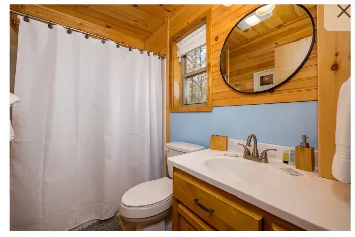 Cozy cabin bathroom with tub/shower, natural light, and toiletries
