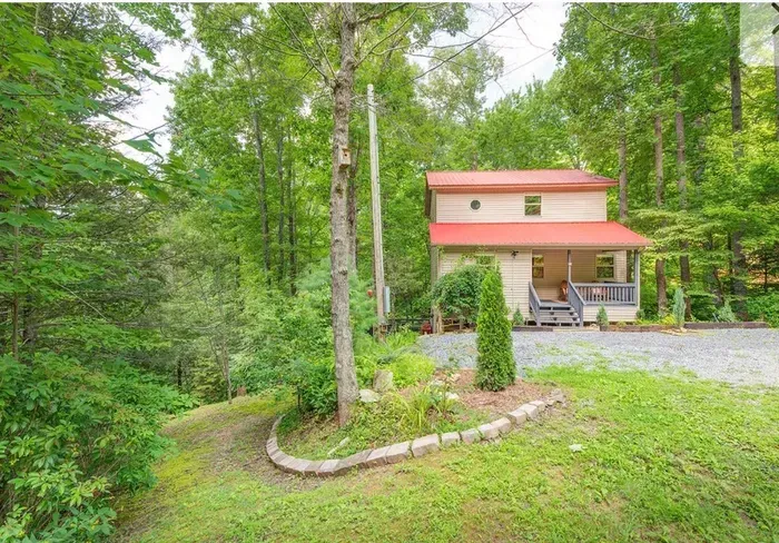 Secluded forest cabin with red roof, porch, and gravel parking