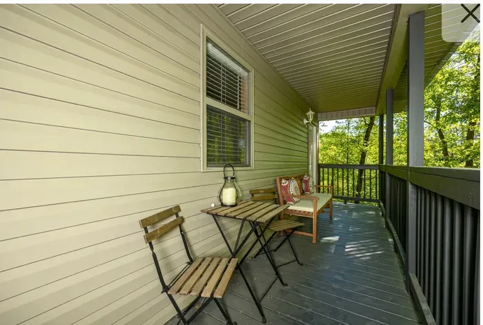Covered porch with bistro set and wooded views—relax outdoors.