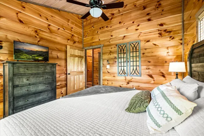Warm, rustic bedroom with TV, ceiling fan, and plush queen bed