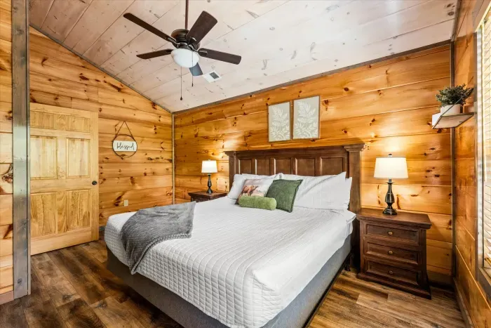 Cozy cabin bedroom with king bed, warm wood walls & ceiling fan