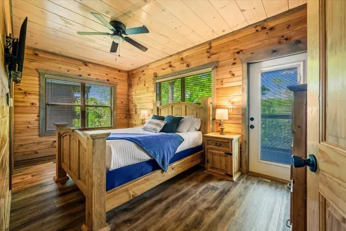 Sunny cabin bedroom with deck access, forest views, and cozy queen bed