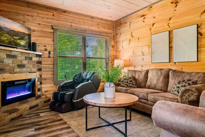 Cozy cabin lounge with fireplace, massage chair, and forest views