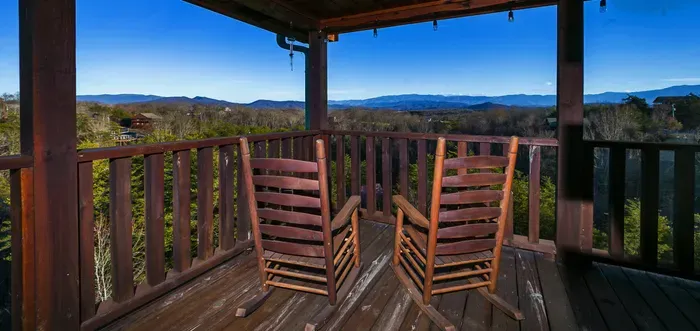 Covered deck with rocking chairs, string lights, and sweeping mountain views