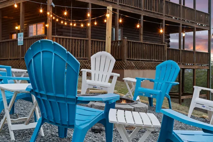Cozy fire pit lounge with Adirondack chairs and string lights by the cabin