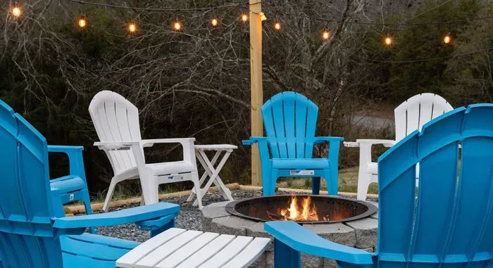 Cozy fire pit lounge with Adirondack chairs, string lights, and woodland views.