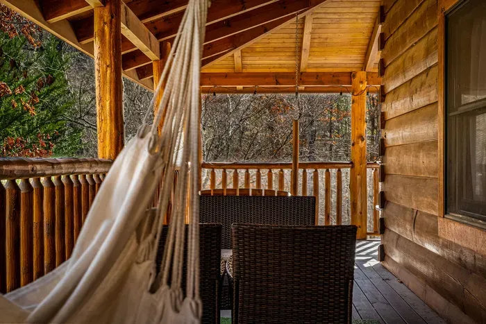 Covered log cabin deck with hammock and dining, serene forest view