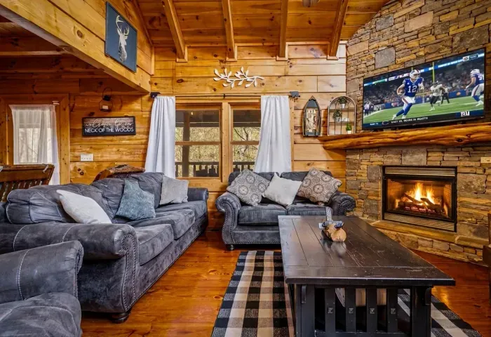 Warm cabin lounge with stone fireplace, vaulted beams, and comfy sofas