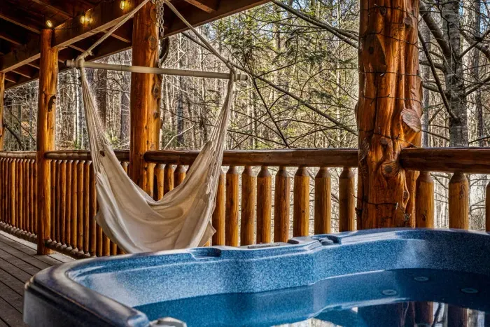 Forest-view deck with hot tub, hammock chair, and cozy string lights