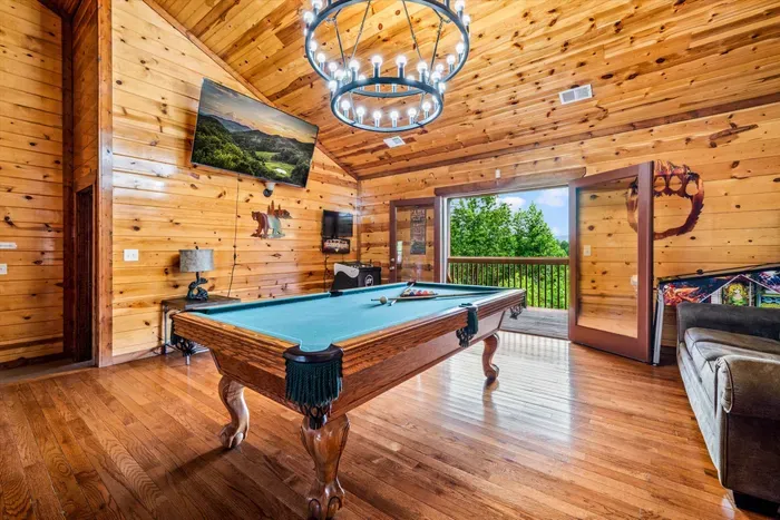 Rustic cabin game room with pool table, TV, and deck views