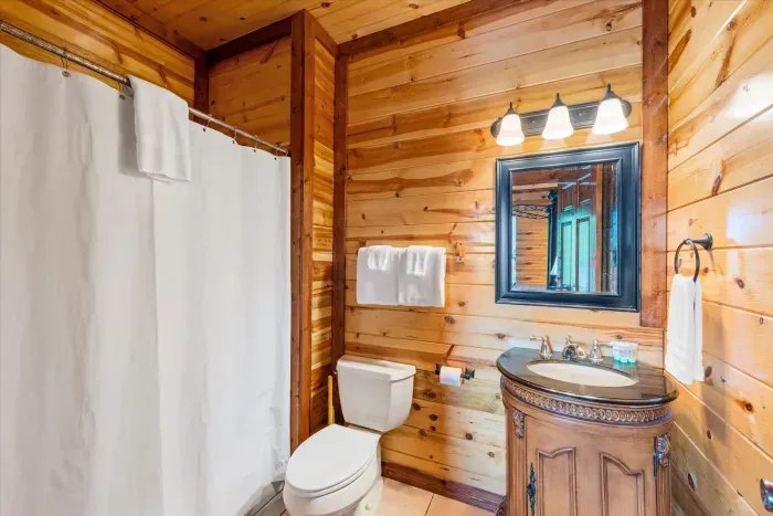 Rustic wood-paneled bathroom with bright vanity and cozy cabin charm