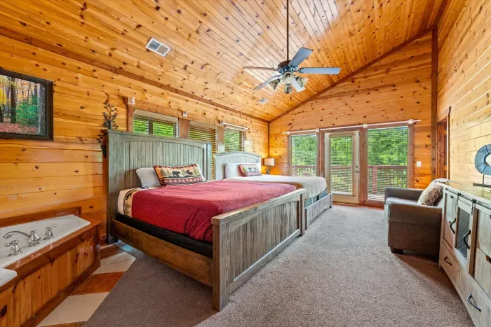 Spacious wood-lined bedroom with two beds, deck access, and soaking tub