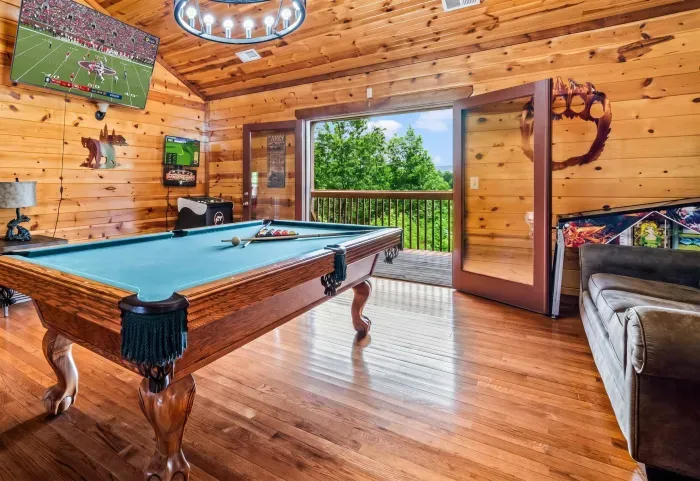 Rustic game room with pool table, arcade, TV, and scenic deck access