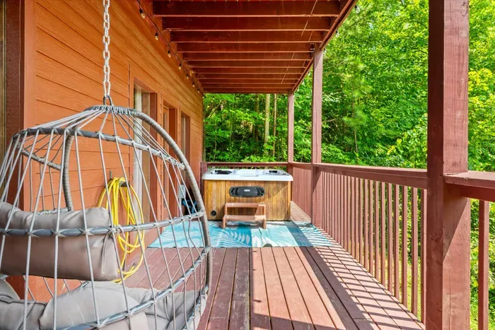 Private covered deck with hot tub and hanging chair in the trees
