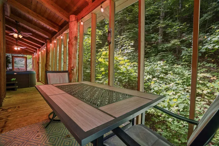 Screened forest porch with dining area, string lights, and hot tub