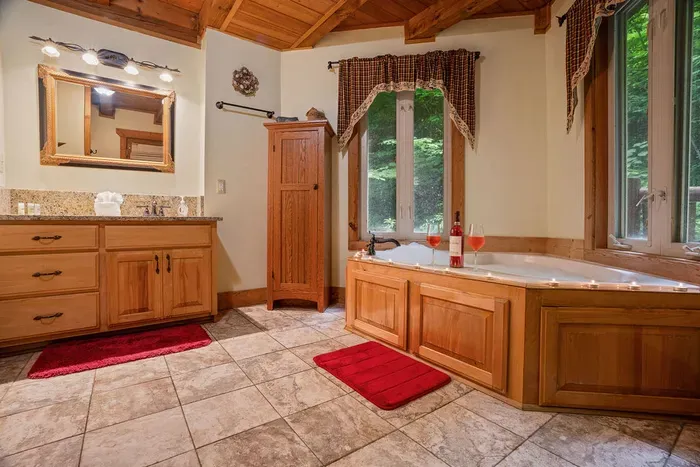 Spa-like bathroom with soaking tub, granite vanity, and forest views