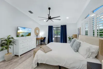 Modern primary bedroom with a stylish workspace, large walk-in closet, TV, resort-style en suite bathroom and direct access to a private outdoor hot tub—ideal for relaxation and remote work.