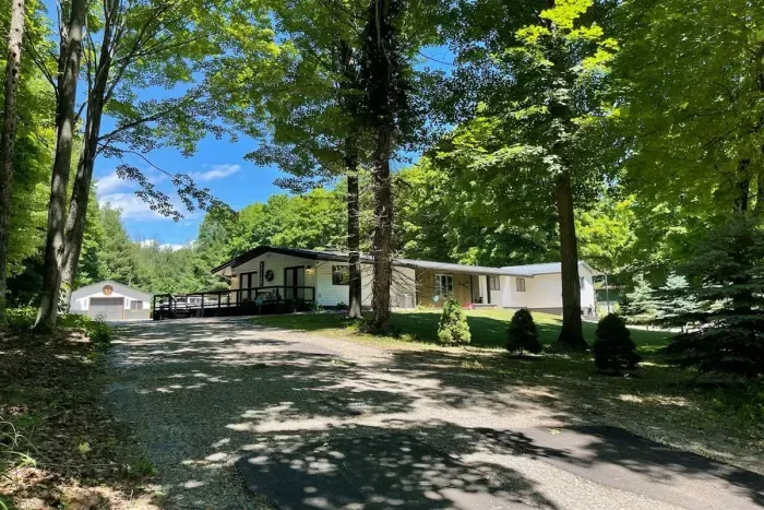 Lake Ann Lodge Driveway view, huge Northwoods Neighborhood lot with soaring hardwoods and pines, wrap around deck side and back with two wheelchair ramps. Multiple entry/exit doors.