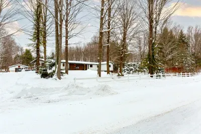 Lake Ann Lodge Driveway view, huge Northwoods Neighborhood lot with soaring hardwoods and pines, wrap around deck side and back with two wheelchair ramps. Multiple entry/exit doors.