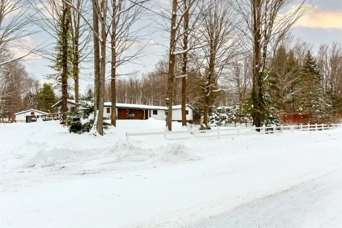 Lake Ann Lodge Driveway view, huge Northwoods Neighborhood lot with soaring hardwoods and pines, wrap around deck side and back with two wheelchair ramps. Multiple entry/exit doors.