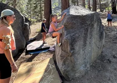 A picture of a little girl bouldering and ehr coach watching in spotting her with a crash pad below.