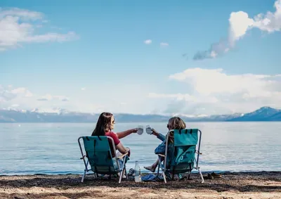 To people sitting in chairs on the beach in front of a lake