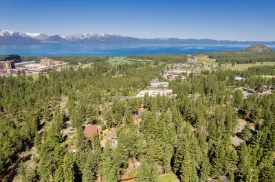 Birdeye view of pine trees, location of The Tahoe Retreat, and Lake Tahoe and snowcapped mountains in the background