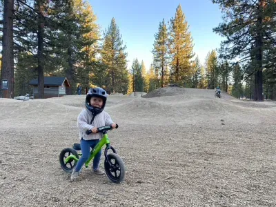 A toddler riding a green strider on a small pump track.