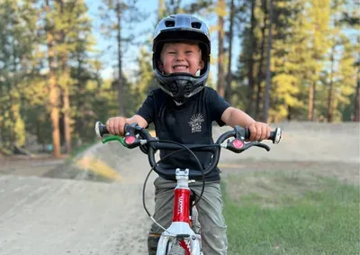 a really happy kid biking on a trail in a black shirt and red bike.