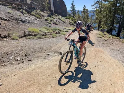 A aoman riding a blue mountain bike working really hard riding up a hill.