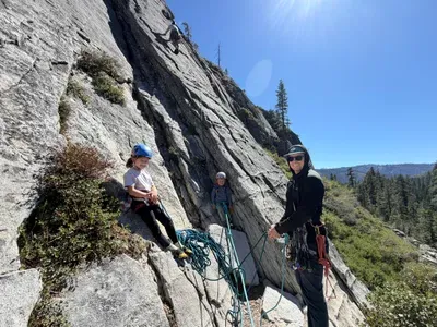 a man and two kids about to start rock climbing up a piece of granite with ropes
