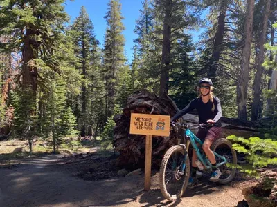 A woman on a mountain bike standing next to a Mr. Toads Wild Ride sign.