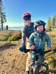 A dad riding a bike with his son sitting on a bike seat in front of him.