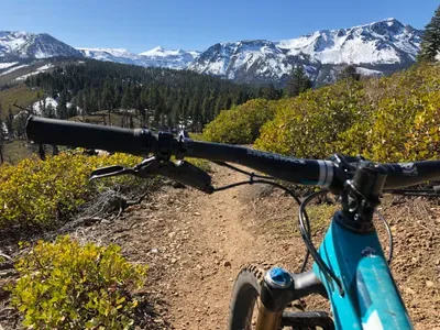 a blue mountain bike and snowy mountains in the background with a trail.