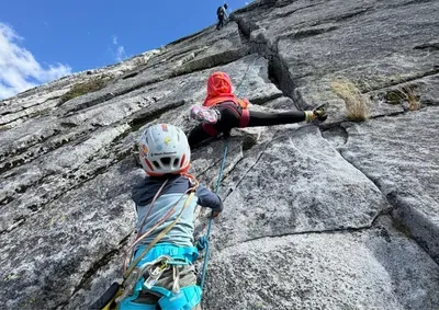 two young climbers in bright colors climbing up a granite wall