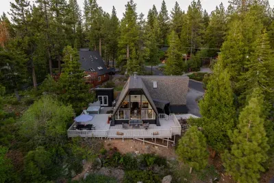 Overhead view of Stuga '66. The wraparound deck is fully outfitted for you! Complete with 6 seat exterior dining table and umbrella, conversation set, cornhole plus other life size games, speaker, and Salt Water Spa tucked under the pines.