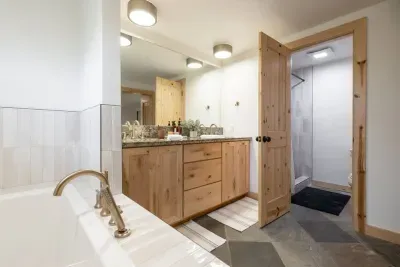View from our primary suite soaking tub. This bath has dual vanity sinks and a newly tiled walk-in shower visible through the open door. We stock all our bathrooms with shampoo, conditioner, body wash, and some extra items from Sparta Candle Co!