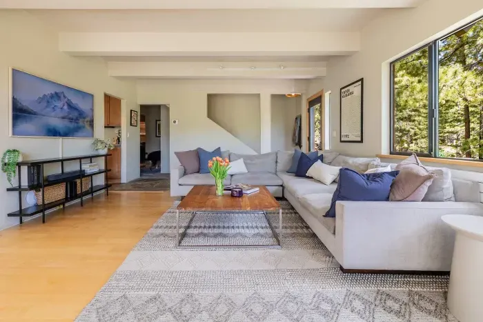 75" flat screen CanvasTV, extra large comfortable sectional, and stunning views from every window. You can see the stairwell to the upstairs just behind the sofa, and the hall on the left leads to the downstairs bedroom, bathroom and laundry room.