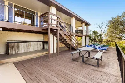 The spacious outdoor deck features picnic tables, lounge chairs, and scenic lake views. A rustic bar under the upper balcony is perfect for casual entertaining and relaxing in the breeze.