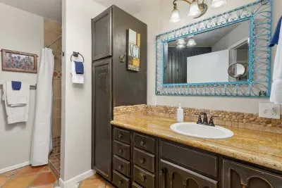 This full bathroom blends rustic warmth with thoughtful amenities, featuring a spacious walk-in shower, a rich wood vanity with ample storage, and a striking gold-toned countertop. 
