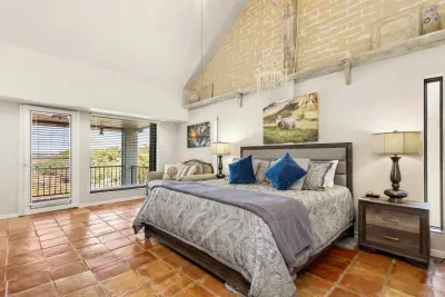 The master bedroom is spacious and airy, featuring a cozy couch near the wide window that frames breathtaking views of the lake, an ideal retreat for rest and relaxation.