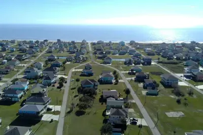 Aerial view of the neighborhood with the Gulf just ahead—an easy walk or quick drive to the beach, with wide-open coastal views and plenty of space to spread out.