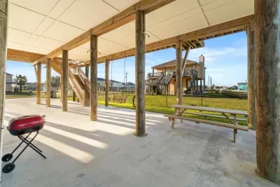 Spacious covered patio with plenty of room to relax, grill, and gather with your group. Enjoy shaded seating at the picnic table, a charcoal grill for cookouts, and an open lawn view—ideal for hanging out after the beach or hosting an outdoor meal.