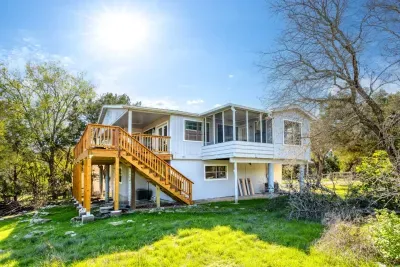 Charming elevated home with a sunny wraparound feel. Enjoy a large wooden staircase leading to screened and open decks, perfect for relaxing among trees and fresh country air while taking in peaceful Hill Country surroundings.