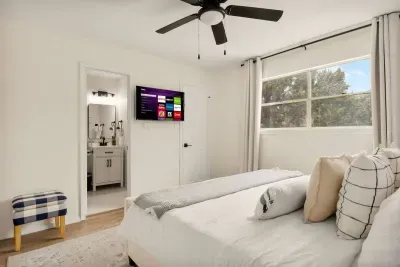 Relax in style in this bright, cream-white bedroom featuring a spacious bed, large window with natural light, and a private bathroom. Enjoy cozy movie nights on the TV or wake up refreshed to the serene views of Mountain Top Retreat.