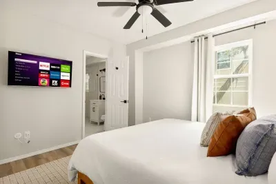 Bright, cozy bedroom featuring a plush bed with layered pillows, smart TV with streaming, and a private en-suite bath. Large window and neutral décor create a relaxing space to unwind after a day of exploring.
