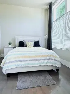 This cozy bedroom offers a comfy retreat with soft linens, plenty of natural light, and windows that let the sunshine in, perfect for relaxing after a long day.