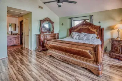 This angle showcases the luxurious bed and matching furniture, set against vaulted ceilings and wood-look flooring. A direct view leads to the en-suite master bathroom, highlighting the spaciousness and privacy of this retreat.