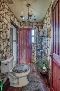 Unique Master Bathroom with rustic stone walls and striking wooden doors. Features include an antique-style chandelier and open metal shelving. A truly distinctive and cozy space next to the master suite.