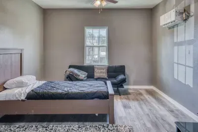 This functional fourth bedroom features one of the Twin beds, a convertible sofa/futon under the window, and a ceiling fan. The room includes a mini-split AC unit for personalized comfort and stylish wood-look flooring.